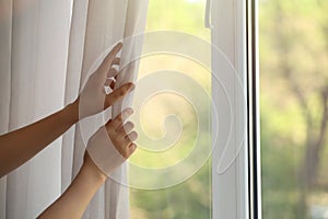 Woman opening white window curtains in room, closeup. Space for text