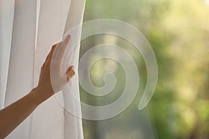 Woman opening white window curtains in room, closeup. Space for text