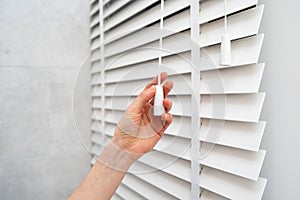 Woman opening window blinds with wooden slats in room