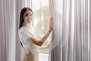 Woman opening window curtain at home in morning