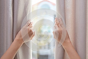 Woman opening window curtains at home