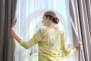 Woman opening window curtains at home