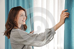 Woman opening window curtains at home