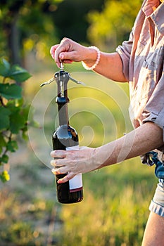 Woman opening wine bottle by corkscrew at vineyard