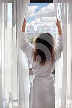 Woman opens curtains and looks up