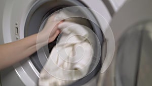 Woman opens door of washing machine, puts in dirty clothes and takes out clothes