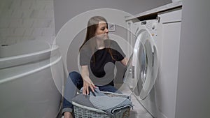 Woman opens door of washing machine, puts in dirty clothes and takes out clothes