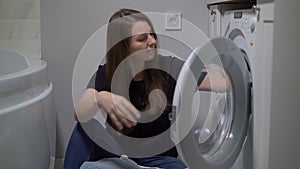 Woman opens door of washing machine, puts in dirty clothes and takes out clothes