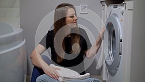 Woman opens door of washing machine, puts in dirty clothes and takes out clothes