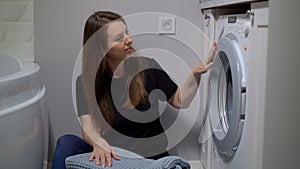 Woman opens door of washing machine, puts in dirty clothes and takes out clothes