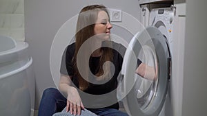 Woman opens door of washing machine, puts in dirty clothes and takes out clothes