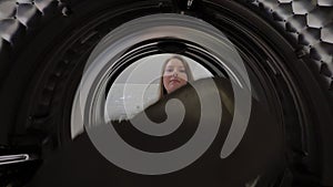 Woman opens door of washing machine, puts in dirty clothes and takes out clothes