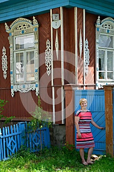 The woman opens a gate to a yard of the wooden house