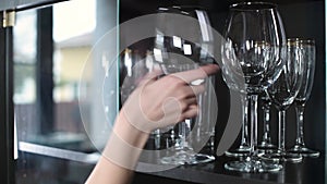 A woman opens a glass cabinet door and takes out a wine glass