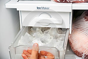 A woman opens an ice maker tray in the freezer to take ice cubes to cool drinks photo