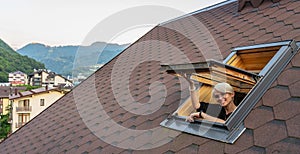 The woman opens and looks out of the attic window overlooking the roof.