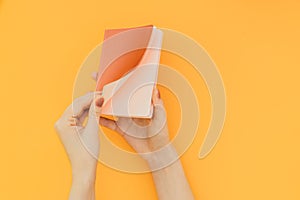 Woman opens a note of coral color on an orange background, hands with notebook a close-up