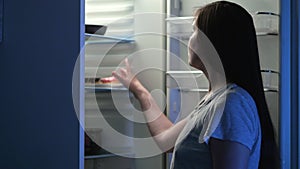 Woman opens refrigerator and looks at tempting donuts