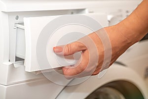 A woman opens the tray for pouring laundry detergent into the washing machine. The concept of washing dirty clothes in a