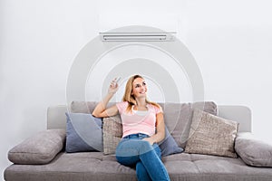 Woman Operating Air Conditioner With Remote Control