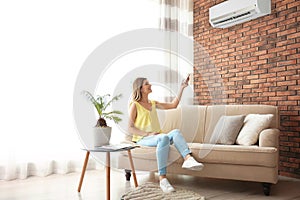 Woman operating air conditioner while sitting on sofa