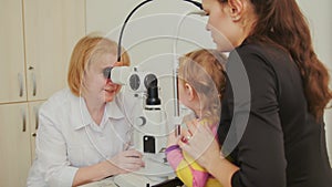 Woman optometrist checks eyesight at little girl - child`s ophthalmology