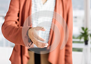 woman with orange blazer giving hand to handshake in her office