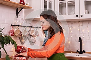 A woman in an orange sweater decorates the house for the new year, Christmas balls and toys, decorating the kitchen