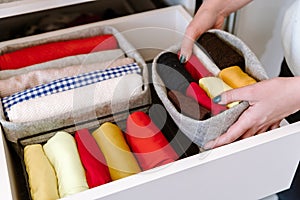 Woman organizing colorful clothes in wardrobe shelves. Minimalist closet