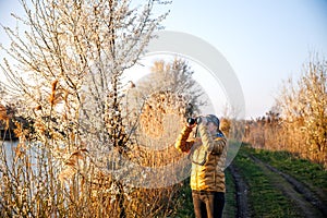 Woman ornithologist with binoculars observes birds arriving at lake in spring