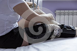 A woman in an orthosis and an elastic bandage after leg surgery sits on a bed in a hospital