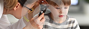 Woman otorhinolaryngologist examines little girl's ear with otoscope in clinic