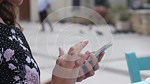 Woman at outdoor cafe using mobile app on smartphone, texting, sending e-mail