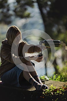 A woman outdoors delights in pouring yerba mate from a thermos into a Mate cup.