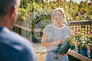 Woman Outdoors In Garden Centre Asking Advice From Sales Assistant Choosing And Buying Rose