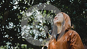 Woman outdoors while it rains. She wears a raincoat. She is very happy, with copy area