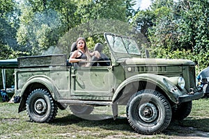 Woman outdoors sitting on hood of military car