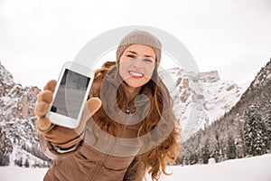 Woman outdoors among snow-capped mountains showing cell phone