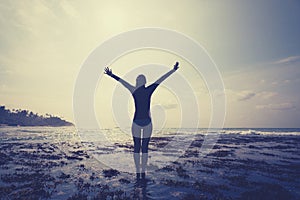 Woman outstretched arms reaching the sky at Sunrise on the seaside reef