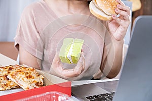 woman over eating fast food burger, pizza and desserts at office desk,