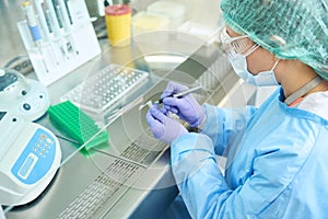 Woman in overalls and protective gloves marks test tubes with biomaterial