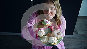 Woman overeat sweet cupcake on kitchen table. Hungry woman eating dessert