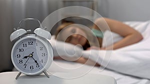 Woman oversleeping in morning, alarm clock ringing near bed, daily routine