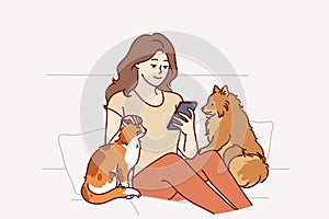 Woman owner of dog and cat sits on couch and plays on phone, enjoying spending time with pets