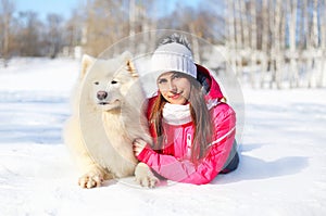 Woman owner with white Samoyed dog lying on snow in winter