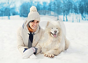 Woman owner with white Samoyed dog lying on snow in winter