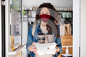 Woman with packed take away food and coffee, looking at camera. Coronavirus concept.