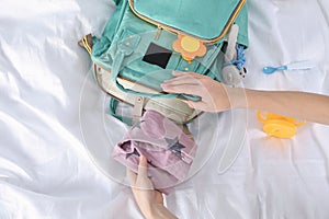 Woman packing baby accessories into maternity backpack on bed