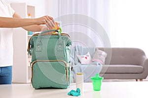 Woman packing baby accessories into maternity backpack on table indoors