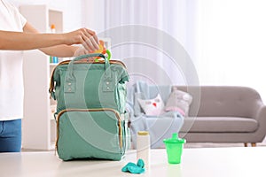 Woman packing baby accessories into maternity backpack on table indoors photo